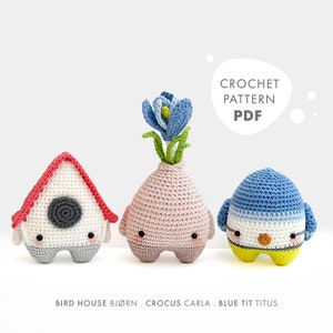 May include: Three crocheted amigurumi toys: a red and white birdhouse, a pink crocus with a blue flower, and a blue tit bird. The toys are all standing on a white background. The text "CROCHET PATTERN PDF" is in a speech bubble above the toys.