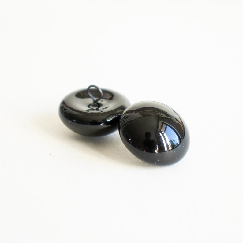 May include: Two black, round, shiny buttons with a metal loop on one button.
