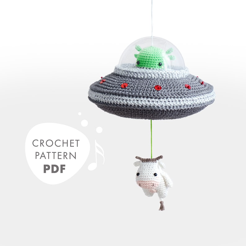 May include: Crochet pattern PDF for a UFO mobile with a green alien and a white cow hanging from it. The UFO is gray with red accents.
