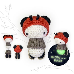 May include: Three crocheted glow-in-the-dark firefly toys. The largest firefly is wearing a brown sweater and has a red and white head. The smaller fireflies are wearing red and white heads. The text "Glow in the Dark" is on a black circle.