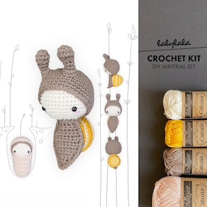 May include: Crochet kit for making a cute snail amigurumi toy. The kit includes four balls of yarn in beige, brown, yellow, and pink. The yarn is labelled "Scheepjes Catona".