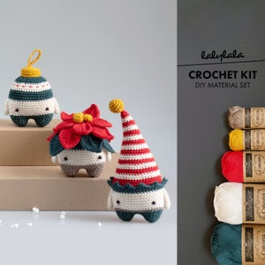 Op de afbeelding: Haakpakket voor het maken van drie amigurumi-versieringen: een groen-witte versiering met een gele ster, een rode kerstster-versiering en een groen-rode elf-versiering. De set bevat garen in verschillende kleuren en een haaknaald.