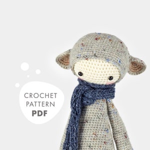 May include: Crochet pattern PDF for a gray and white amigurumi doll with blue scarf. The doll has a speckled gray hat and brown ears.