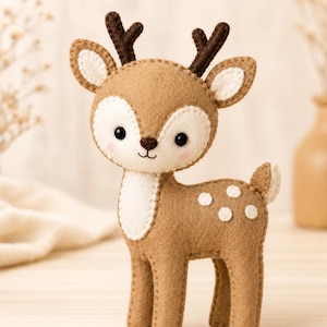 May include: A handcrafted felt deer figurine featuring a light brown body with cream-coloured accents on the face, chest, and ears. It has dark brown antlers, black bead eyes, a stitched nose and mouth, and white circular spots on its side.