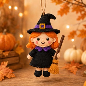 May include: A felt hanging ornament shaped like a witch with orange hair, wearing a black dress with a purple collar and a matching black pointed hat with a purple band and yellow buckle. The figure holds a small brown broom with orange bristles.