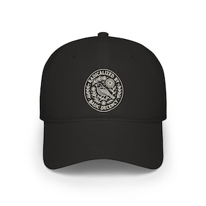 Könnte beinhalten: Schwarze Baseballkappe mit weißem, kreisförmigem Grafikdesign. Das Design zeigt einen Vogel, Blumen und die Worte "RADICALIZED BY BASIC DECENCY" in einem kreisförmigen Design. Die Kappe hat einen gebogenen Schirm.