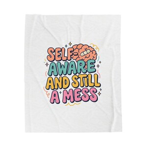 Könnte beinhalten: Weiße Decke mit dem Text "SELF AWARE AND STILL A MESS" in bunten Buchstaben. Das Design beinhaltet ein Cartoon-Gehirn mit einem Pflaster. Die Decke ist ein weiches, gemütliches Produkt.