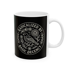 Könnte beinhalten: Weißer Keramikbecher mit schwarzer Außenseite. Das Design ist ein weißes kreisförmiges Emblem mit einem Vogel, Blumen und dem Text "RADICALIZED BY BASIC DECENCY".