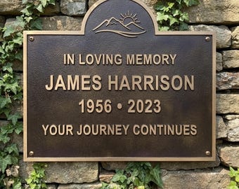 May include: A rectangular bronze memorial plaque with an arched top featuring a mountain and sun graphic. The text reads IN LOVING MEMORY, JAMES HARRISON, 1956-2023, and YOUR JOURNEY CONTINUES in raised, metallic lettering.