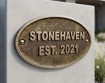 May include: An oval-shaped metal plaque with a weathered bronze finish, featuring the raised text "STONEHAVEN" and "EST. 2021" in a metallic gold tone. The plaque is secured with two visible screws on the left and right sides.