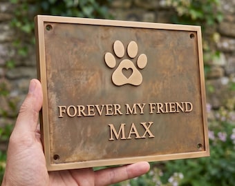 May include: A rectangular bronze-colored metal plaque featuring a raised paw print icon with a heart cutout in the center. The text "FOREVER MY FRIEND" is embossed above the name "MAX" in a clean, sans-serif font. Four corner holes are visible.