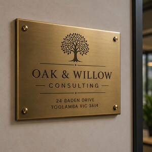 May include: A rectangular brushed brass sign with four corner mounting screws. It features a tree icon above the text OAK & WILLOW CONSULTING and the address 24 BADEN DRIVE TOOLAMBA VIC 3614, all engraved in a dark, bold, sans-serif font.