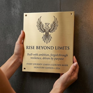 May include: A rectangular brushed gold metal plaque featuring a black engraved phoenix graphic at the top. The text reads: RISE BEYOND LIMITS, Built with ambition, forged through resilience, driven by purpose, EVERY JOURNEY LEAVES A GOLDEN MARK, SIGNATURE EDITION 2024.
