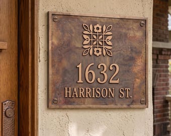 May include: A rectangular bronze-toned metal house address plaque featuring a mottled patina finish. The plaque displays a symmetrical floral motif above the number 1632 and the text HARRISON ST. It is secured with four visible corner screws.