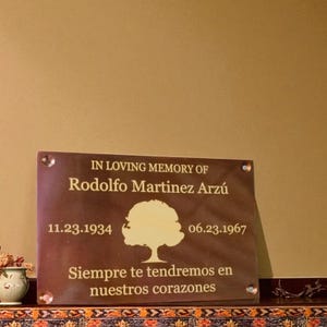 May include: A rectangular brown memorial plaque featuring the text IN LOVING MEMORY OF Rodolfo Martinez Arz&uacute;, the dates 11.23.1934 and 06.23.1967, a central tree graphic, and the Spanish text Siempre te tendremos en nuestros corazones.