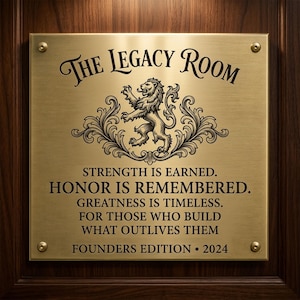 May include: A rectangular brushed brass plaque with four corner screws, featuring the text THE LEGACY ROOM above a central lion emblem. Below, the text reads: STRENGTH IS EARNED. HONOR IS REMEMBERED. GREATNESS IS TIMELESS. FOR THOSE WHO BUILD WHAT OUTLIVES THEM. FOUNDERS EDITION &bull; 2024.