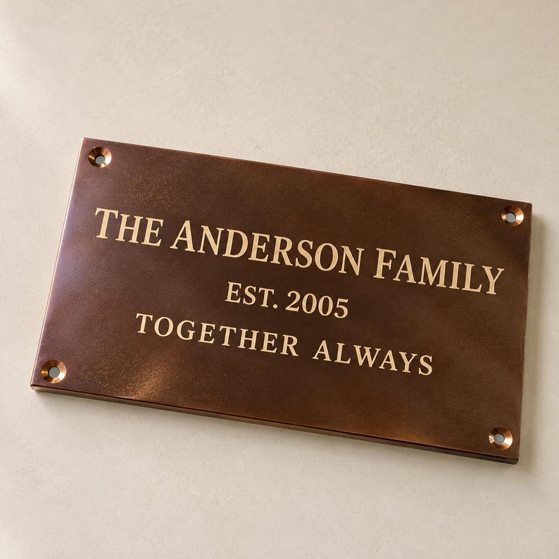 May include: A rectangular bronze-toned metal plaque featuring the engraved text THE ANDERSON FAMILY, EST. 2005, and TOGETHER ALWAYS. The plaque has a smooth, dark finish with four circular mounting holes, one located in each of the four corners.
