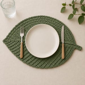 May include: A green, leaf-shaped crochet placemat with a white plate, fork, and knife. The fork and knife have wooden handles. A clear glass of water is in the upper left corner. The placemat is on a beige surface.