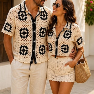 May include: Matching crochet shirt and shorts set in cream with black floral accents. The shirt has a button-down front and short sleeves. The shorts have pockets. A woven handbag completes the look. The set is worn by two people.