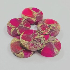 May include: A collection of six round, polished stones. The stones feature a vibrant mix of colors, including deep pink, burgundy, and gold. The stones have a mosaic-like pattern, with each piece displaying a unique arrangement of colors and textures. The stones are likely for jewelry making.