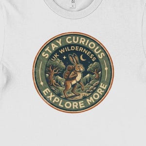 May include: White t-shirt with a circular graphic. The design features a rabbit with a backpack, trees, and the text "Stay Curious UK Wilderness Explore More." The graphic is in brown, green, and blue.