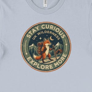 May include: Light blue t-shirt featuring a circular graphic with a fox carrying a backpack and walking with a staff. The graphic reads "Stay Curious UK Wilderness Explore More" in a circular design with mountains and a crescent moon.