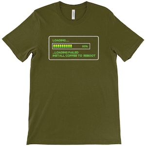 May include: An olive green short-sleeve t-shirt featuring a white rectangular graphic with a loading bar at 50% and the text: LOADING..... ...LOADING FAILED INSTALL COFFEE TO REBOOT. The design is printed in a bright lime green color.