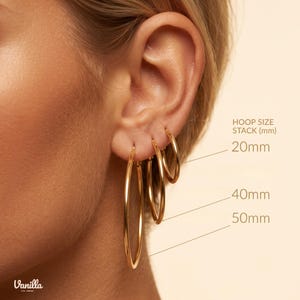 Pode incluir: Três brincos de argola dourados de tamanhos variados em uma orelha. O texto HOOP SIZE STACK (mm) é visível com etiquetas de 20mm, 40mm e 50mm apontando para cada argola. A menor mede 20mm, a média 40mm e a maior 50mm.