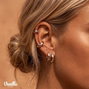 Peut inclure: Un ensemble de quatre boucles d'oreilles et bagues d'oreille en argent poli. Deux petits anneaux sont placés sur le lobe, tandis que deux bagues lisses et arrondies sont fixées sur le cartilage. Le texte Vanilla 1978 JEWELRY est visible.