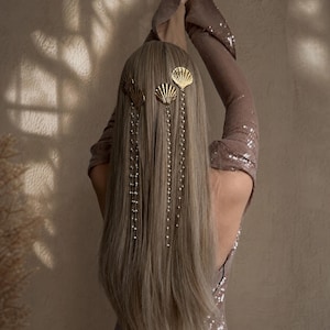Könnte beinhalten: Ein Set aus goldfarbenen Haaraccessoires mit muschelförmigen Clips und langen, herabhängenden Ketten, die mit kleinen weißen Perlen verziert sind. Die Haarspangen sind in langem, glattem, hellbraunem Haar befestigt, wobei die Ketten herabhängen.