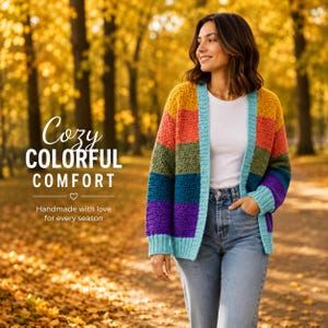 May include: A long-sleeved, open-front crochet cardigan featuring horizontal stripes in mustard yellow, orange, olive green, purple, and light blue. The garment is worn over a plain white t-shirt and light-wash blue denim jeans.