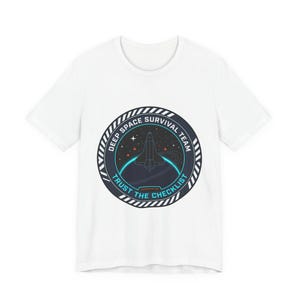 May include: White t-shirt with a circular emblem. The emblem features a spaceship, stars, and the text "DEEP SPACE SURVIVAL TEAM" and "TRUST THE CHECKLIST". The design is in navy blue, teal, and white.