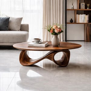 Puede incluir: Una taza de cerámica blanca con asa negra y el texto "But First, Coffee" en negrita negra. La taza se encuentra sobre un fondo borroso, sugiriendo un ambiente acogedor.