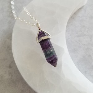May include: A silver chain necklace with a purple, green and white fluorite crystal pendant. The pendant is in the shape of a point and is set in a silver bezel.