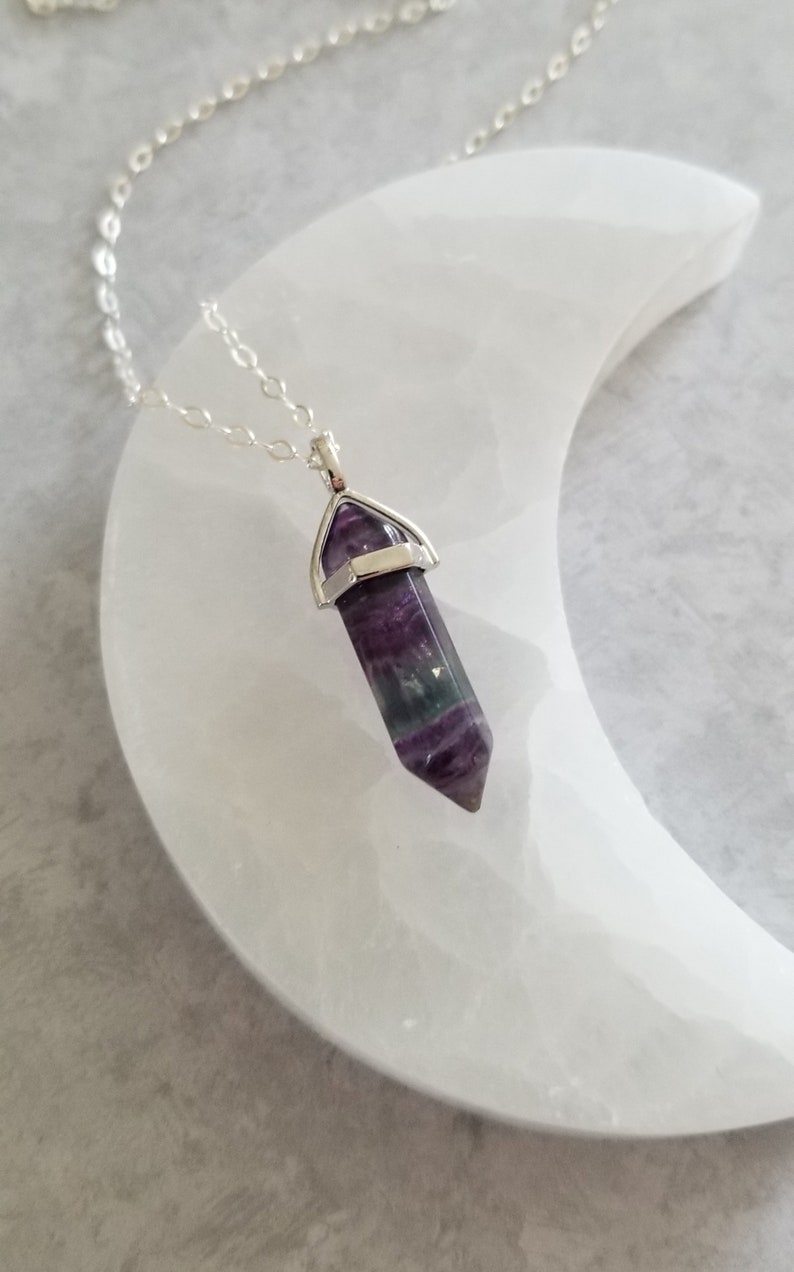 May include: A silver chain necklace with a purple, green and white fluorite crystal pendant. The pendant is in the shape of a point and is set in a silver bezel.