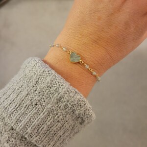 May include: A gold chain bracelet with a light blue heart-shaped charm and small light blue beads.