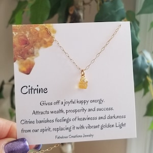 May include: A gold chain necklace with a small, raw citrine crystal pendant. The necklace comes with a card that reads "Citrine Gives off a joyful happy energy. Attracts wealth, prosperity and success. Citrine banishes feelings of heaviness and darkness from our spirit, replacing it with vibrant golden Light Fabulous Creations Jewelry"