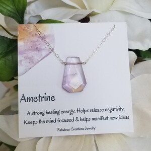 May include: Ametrine necklace with a purple and orange crystal pendant. The necklace is on a white card with the text "Ametrine", "A strong healing energy. Helps release negativity. Keeps the mind focused & helps manifest new ideas", and "Fabulous Creations Jewelry".