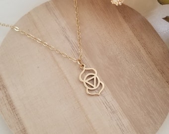 May include: A gold necklace with a delicate chain and a pendant featuring the symbol for the sacral chakra. The necklace is displayed on a wooden surface.