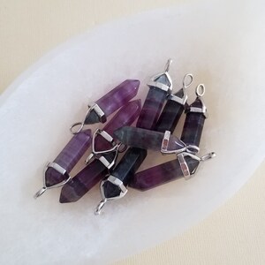 May include: A group of eight purple and green fluorite crystal point pendants with silver-toned metal caps and loops.