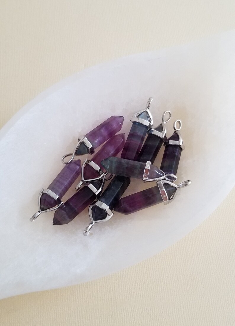 May include: A group of eight purple and green fluorite crystal point pendants with silver-toned metal caps and loops.