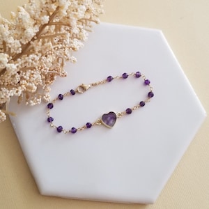 May include: A delicate gold chain bracelet with small purple amethyst beads and a heart-shaped amethyst pendant.