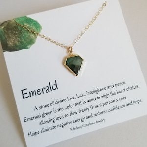 May include: A gold chain necklace with a green emerald gemstone pendant. The card reads "Emerald. A stone of divine love, luck, intelligence and peace. Emerald green is the color that is used to align the heart chakra, allowing love to flow freely from a person's core. Helps eliminate negative energy and restore confidence and hope. Fabulous Creations Jewelry"