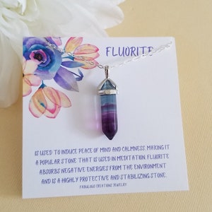 May include: A silver chain necklace with a purple and blue fluorite crystal pendant. The pendant is shaped like a point and has a silver cap. The necklace comes with a card that reads "Fluorite is used to induce peace of mind and calmness. Making it a popular stone that is used in meditation. Fluorite absorbs negative energies from the environment and is a highly protective and stabilizing stone. Fabulous Creations Jewelry."