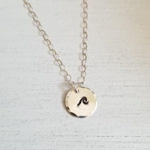 May include: A silver chain necklace with a hammered silver disc pendant featuring a wave design.