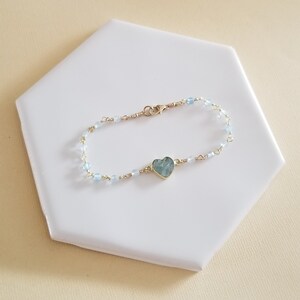 May include: A delicate gold chain bracelet with light blue beads and a heart-shaped aquamarine pendant.