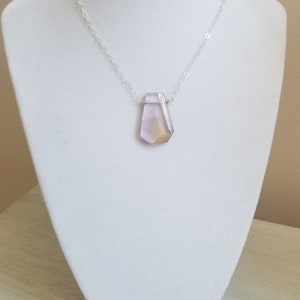 May include: A silver chain necklace with a large, faceted, light purple and yellow gemstone pendant.