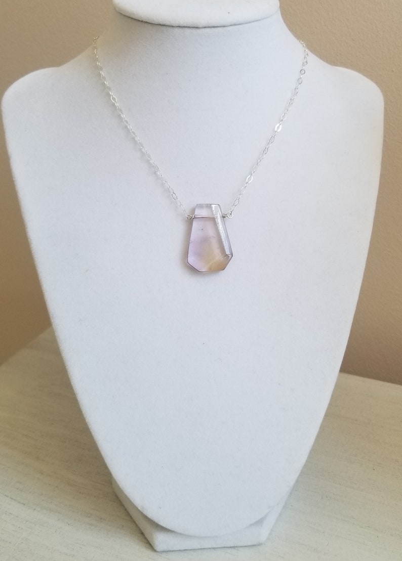 May include: A silver chain necklace with a large, faceted, light purple and yellow gemstone pendant.