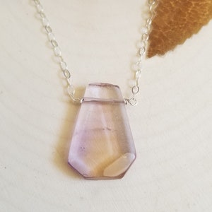 May include: A delicate silver chain necklace with a faceted, light purple gemstone pendant.