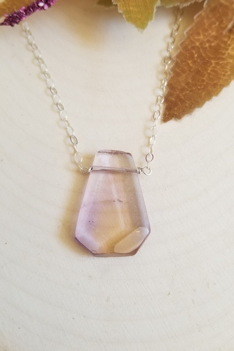 May include: A delicate silver chain necklace with a faceted, light purple gemstone pendant.